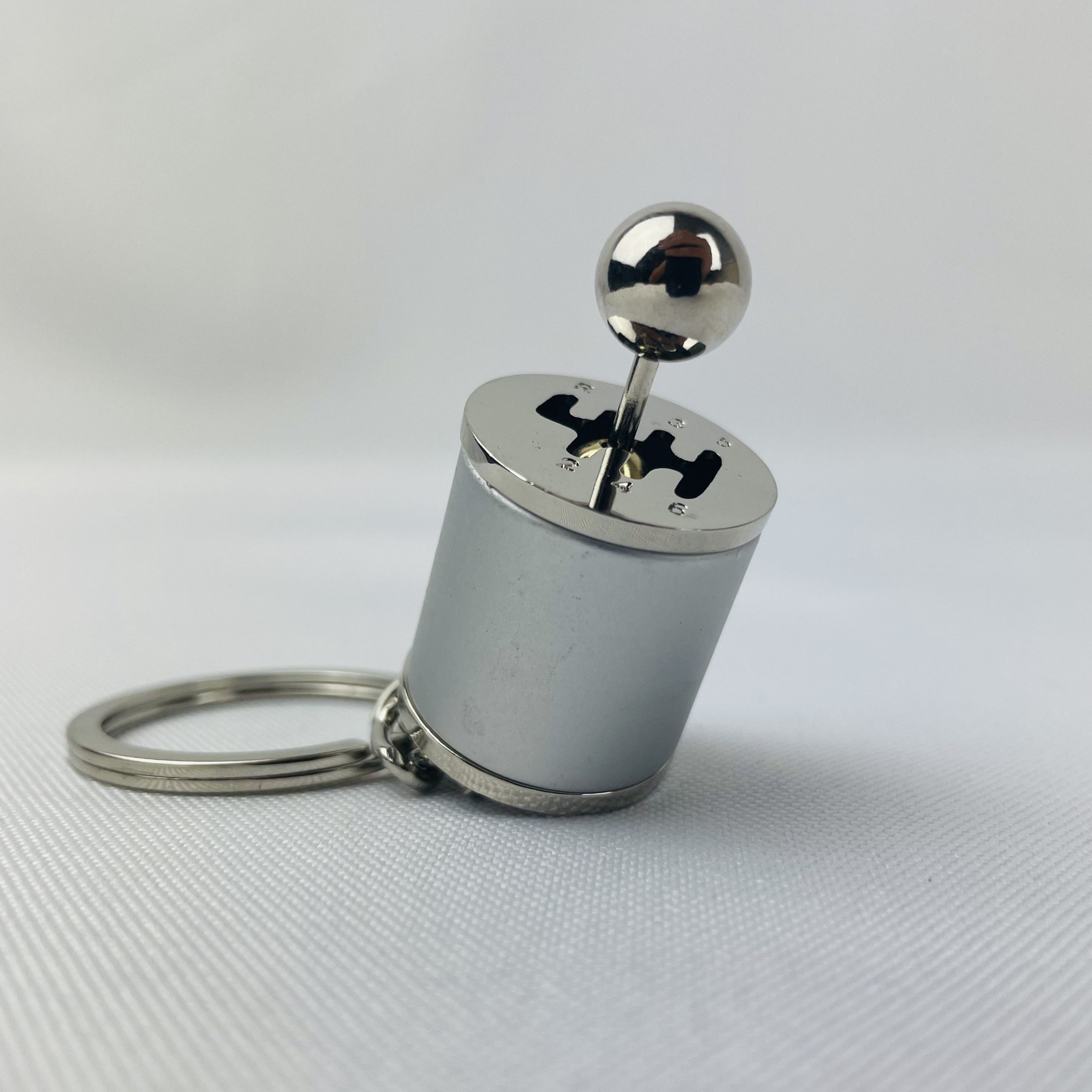 A 6 speed silver manual gear-shifter keychain. You are able to shift into every gear. Displayed sitting up with a white background.